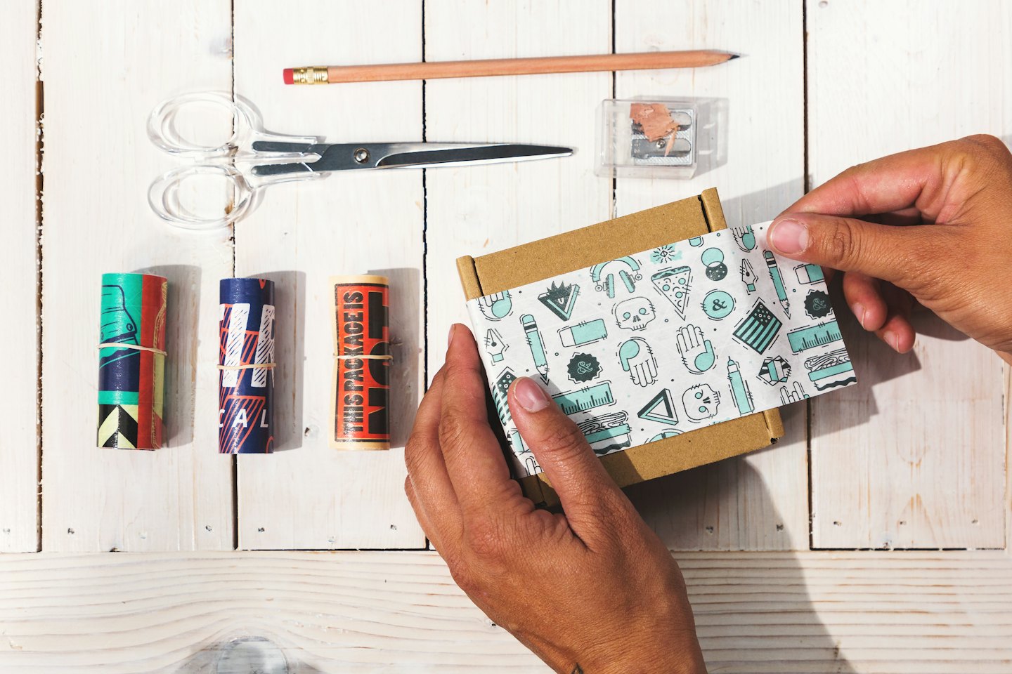 Hands carefully wrapping a small box with patterned tissue paper.